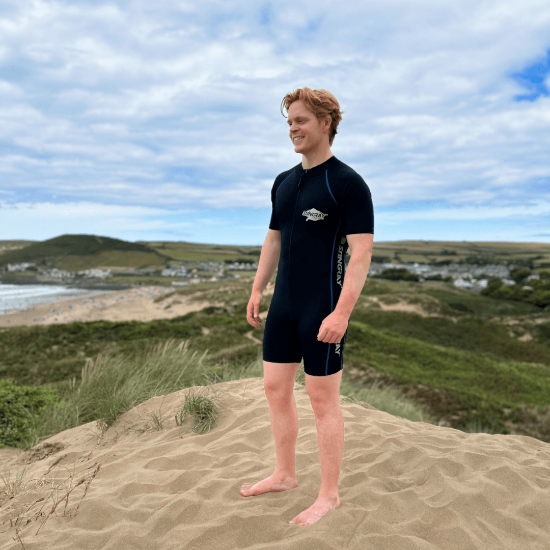 Person wearing a black UPF 50+ sport swimsuit standing on a sandy dune with a scenic landscape in the background.
