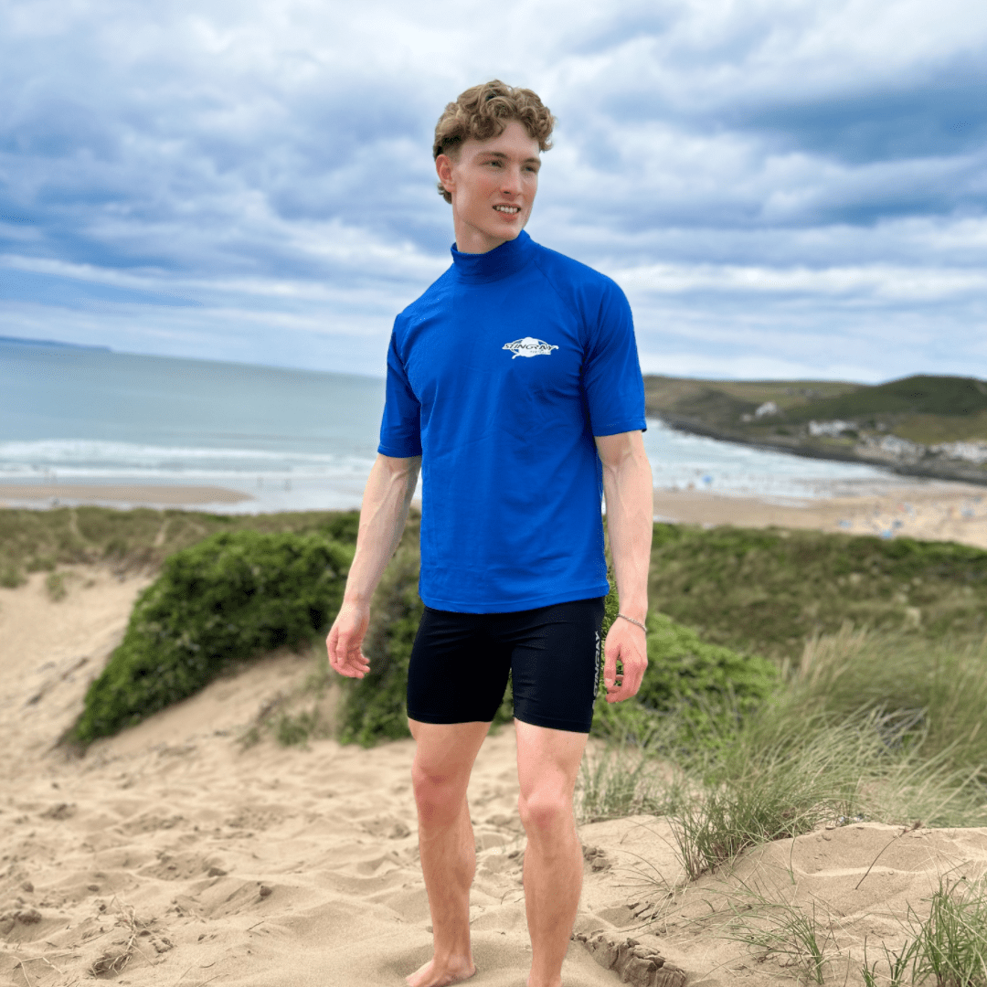 Person wearing a blue UPF50+ rash shirt and UPF 50 swim shorts on a beach