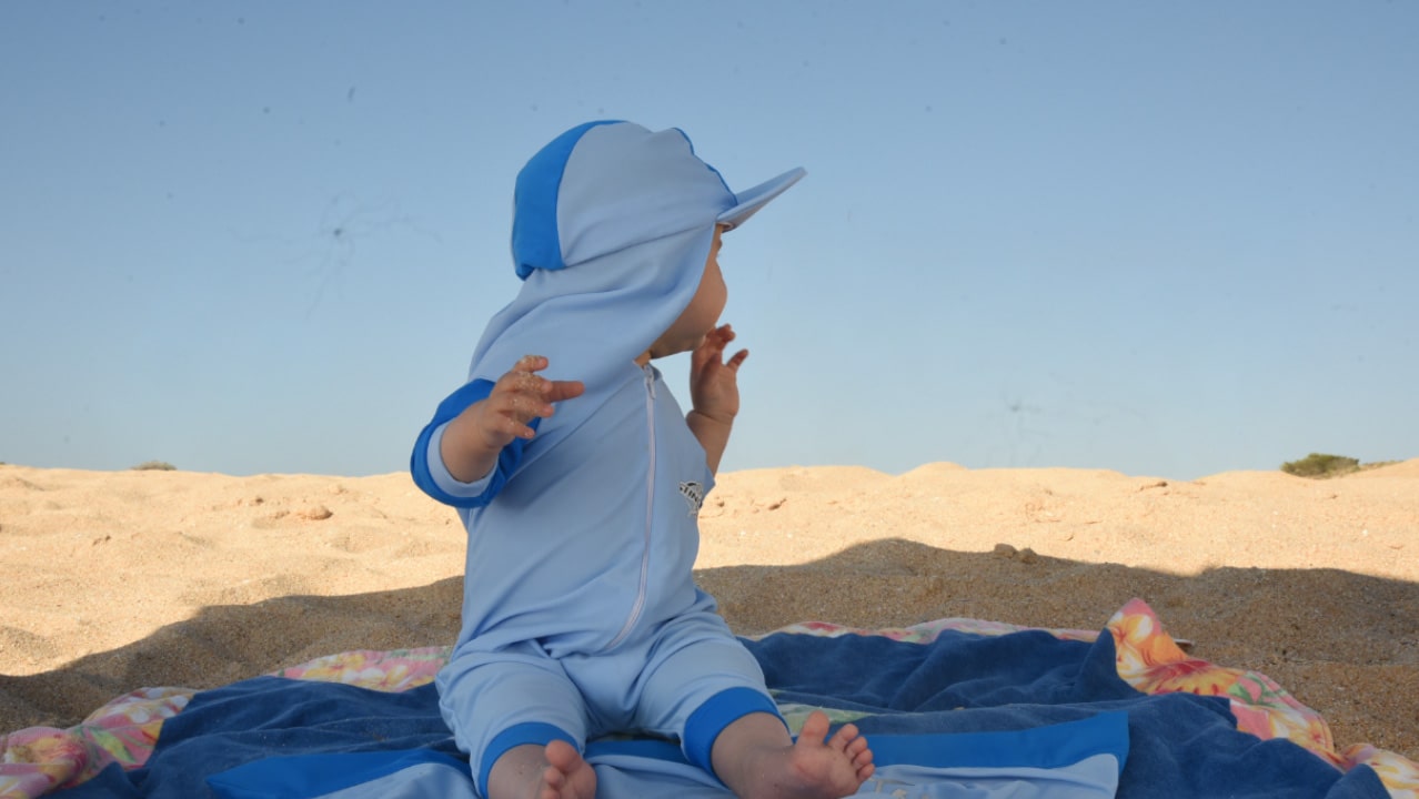 Banner photo of a baby wearing upf 50 sunsuit on the beach for our infant (beachwear) UV protection swimwear and clothing