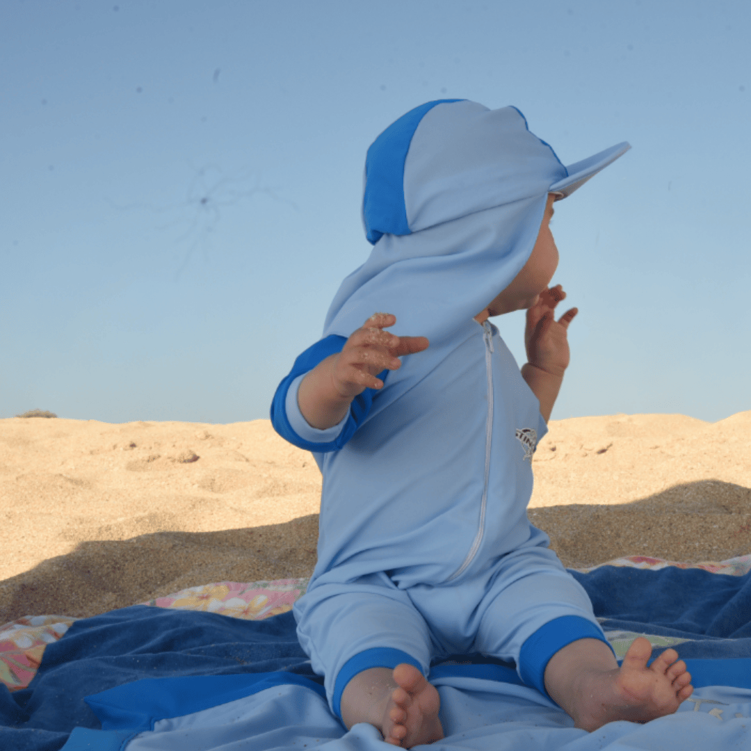 Baby wearing sunsuit and sun hat on the beach