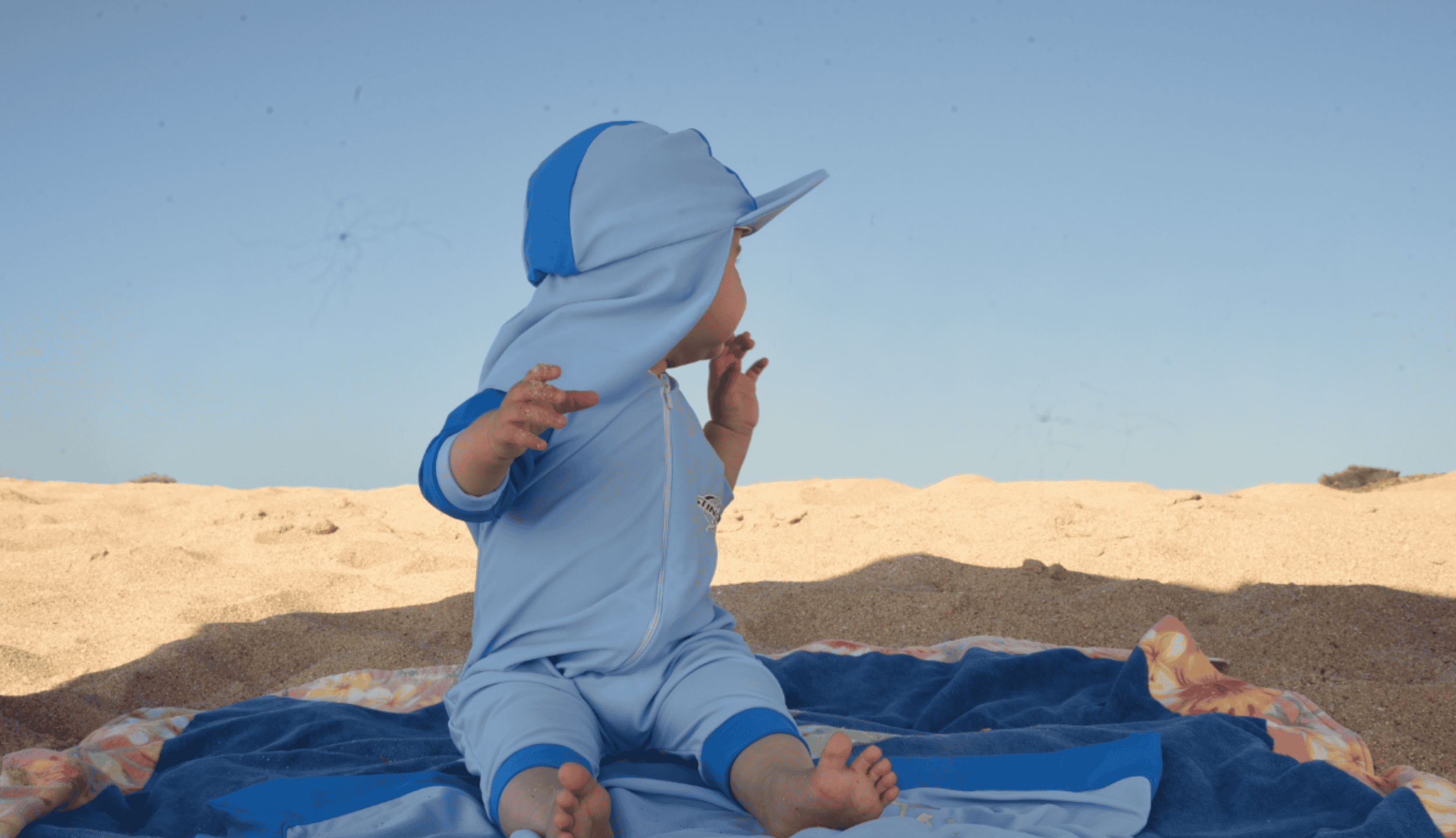 Baby wearing upf 50 sunsuit on the beach