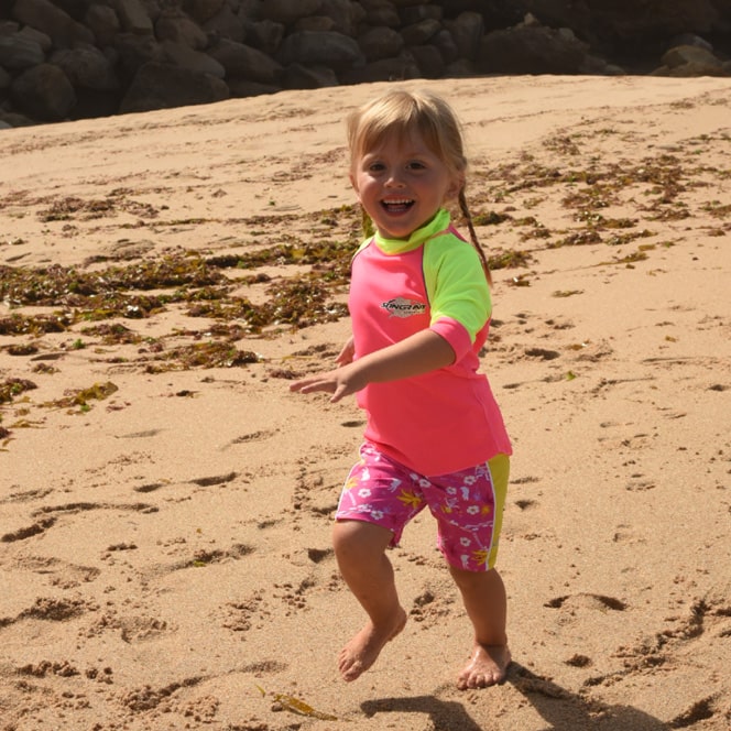 Child running on beach wearing UPF swim shorts in hawaii style print