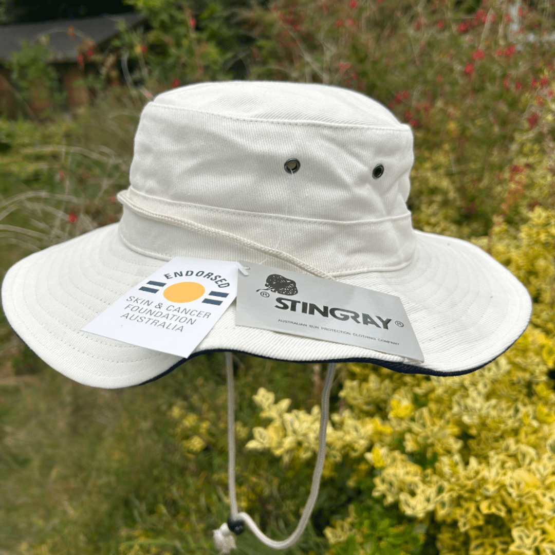 White upf 50+ kids cricket hat with Stingray branding and a tag on a natural background