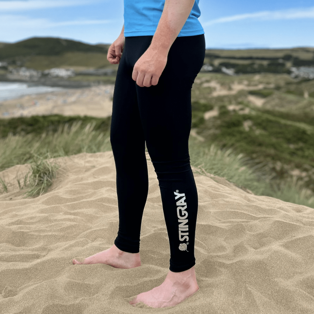 Man wearing black Stingray leggings on a sandy beach with grassy dunes and water in the background.