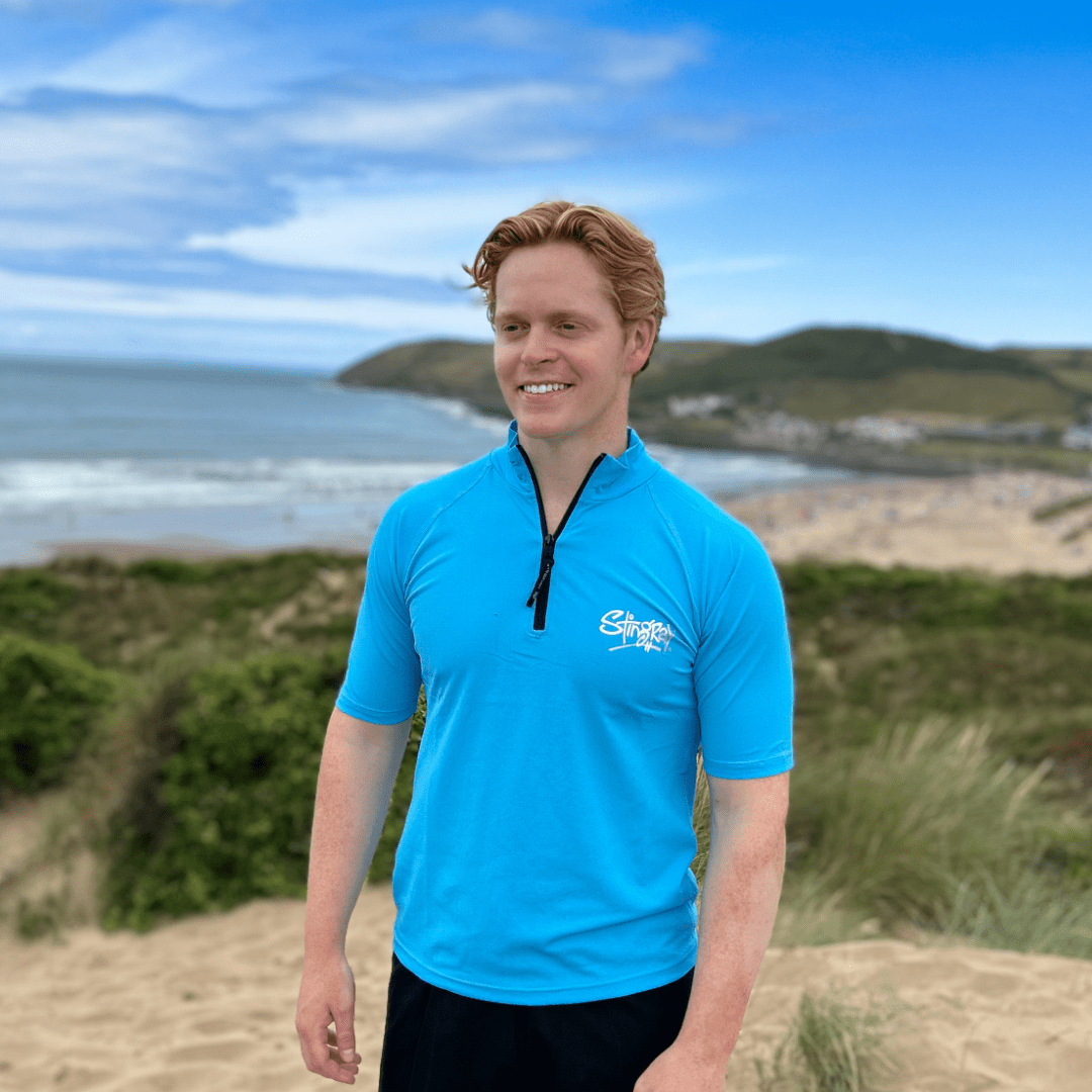 Man wearing a blue upf 50 zipped rash shirt with stingray logo on a beach