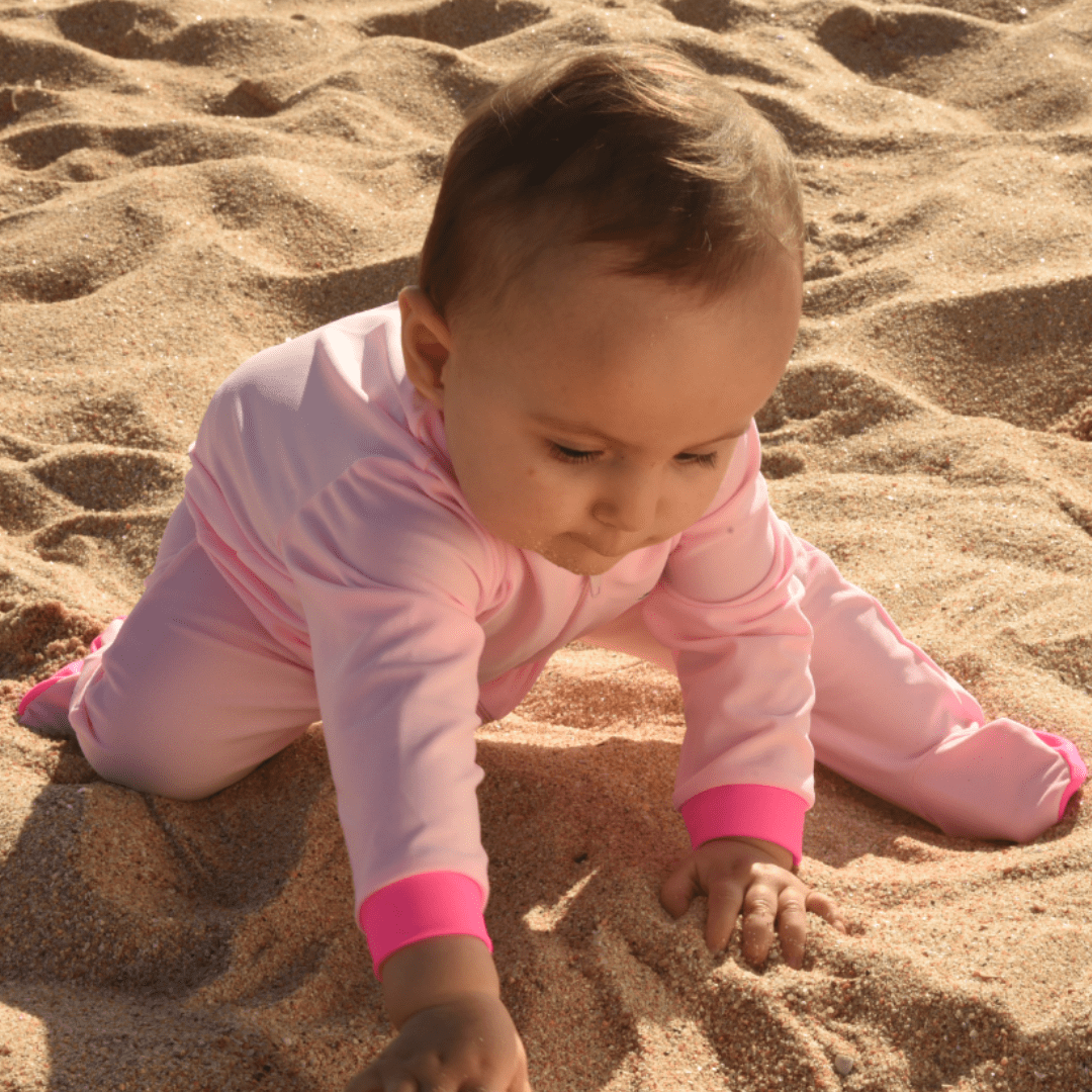 Child in pink UPF 50+ full-body swimsuit playing in sand