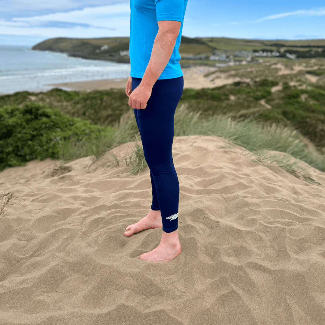 Person wearing blue top and navy UPF 50+ leggings standing on a sandy dune with a beach and ocean in the background.