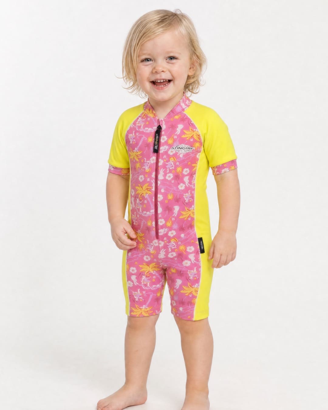 2 year old toddler wearing short sleeve UV sunsuit UPF 50+ in floral and yellow in a white studio 
