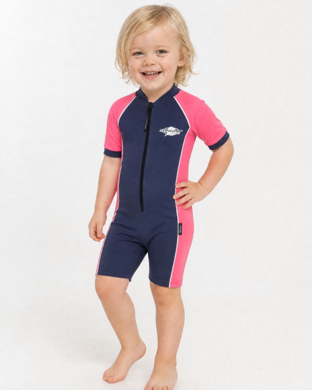 2 year old toddler wearing short sleeve UV sunsuit UPF 50+ in navy and pink in a white studio 