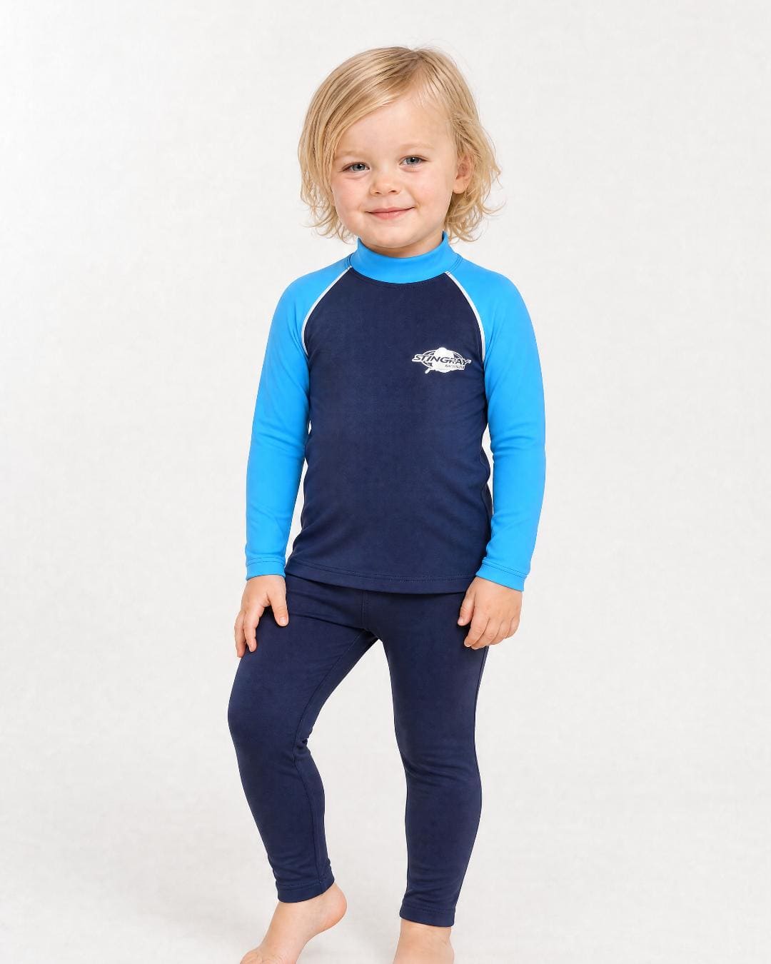 2 year old toddler/child wearing long-sleeve UV rash shirt UPF 50+ in navy and blue, standing in a white studio