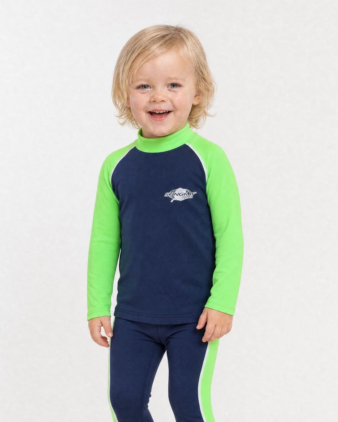 2 year old toddler/child wearing long-sleeve UV rash shirt UPF 50+ in navy and green, standing in a white studio 