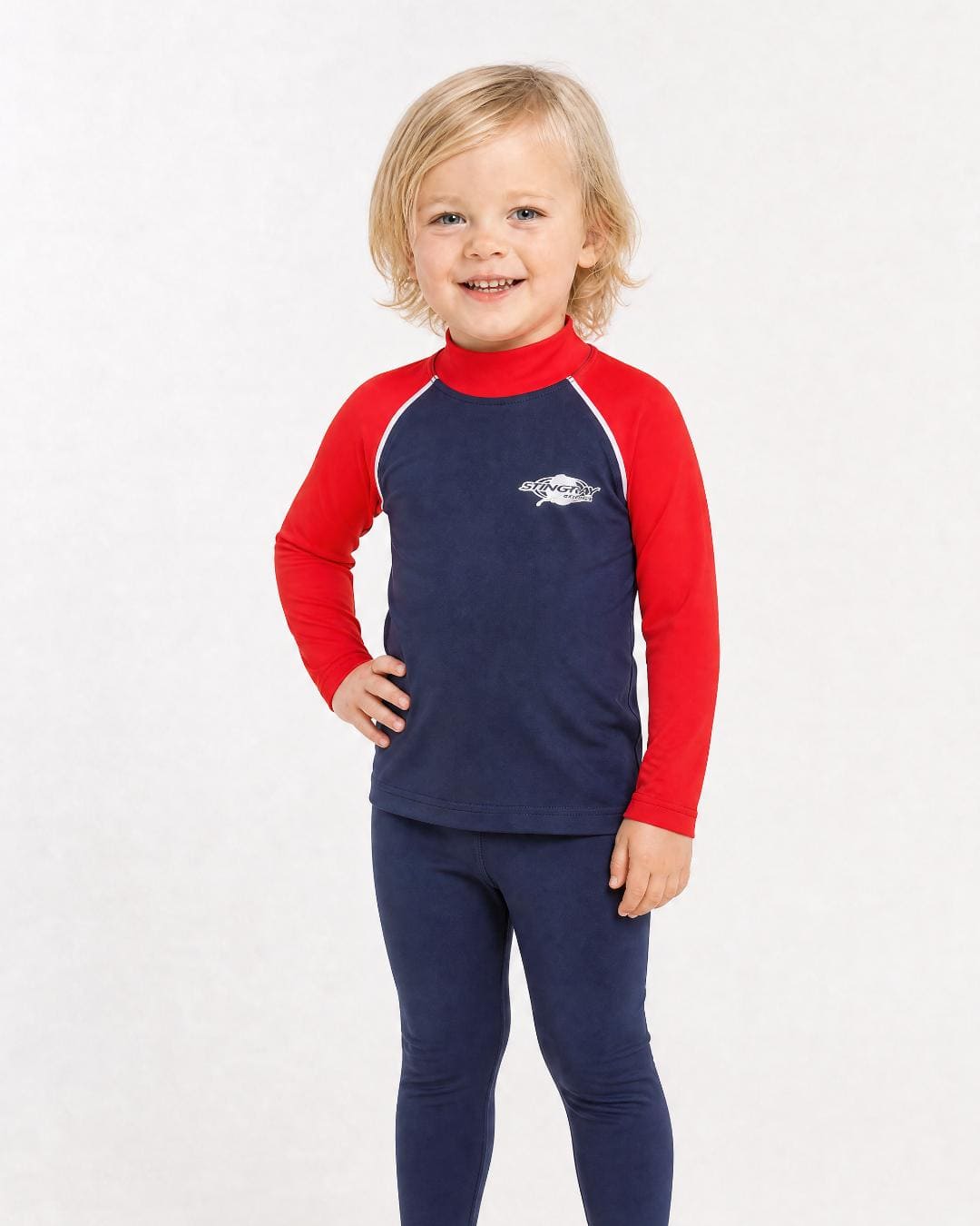 2 year old toddler/child wearing long-sleeve UV rash shirt UPF 50+ in navy and red, standing in a white studio 
