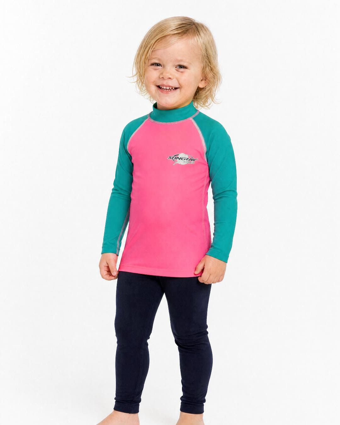 2 year old toddler/child wearing long-sleeve UV rash shirt UPF 50+ in pink and teal, standing in a white studio 