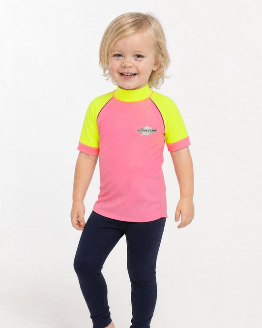2 year old wearing a short sleeve UV swim shirt UPF 50+ in pink and yellow in a white studio
