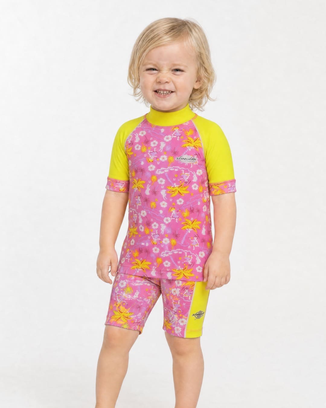 2 year old wearing a short sleeve UV swim shirt UPF 50+ in floral pattern and yellow in a white studio