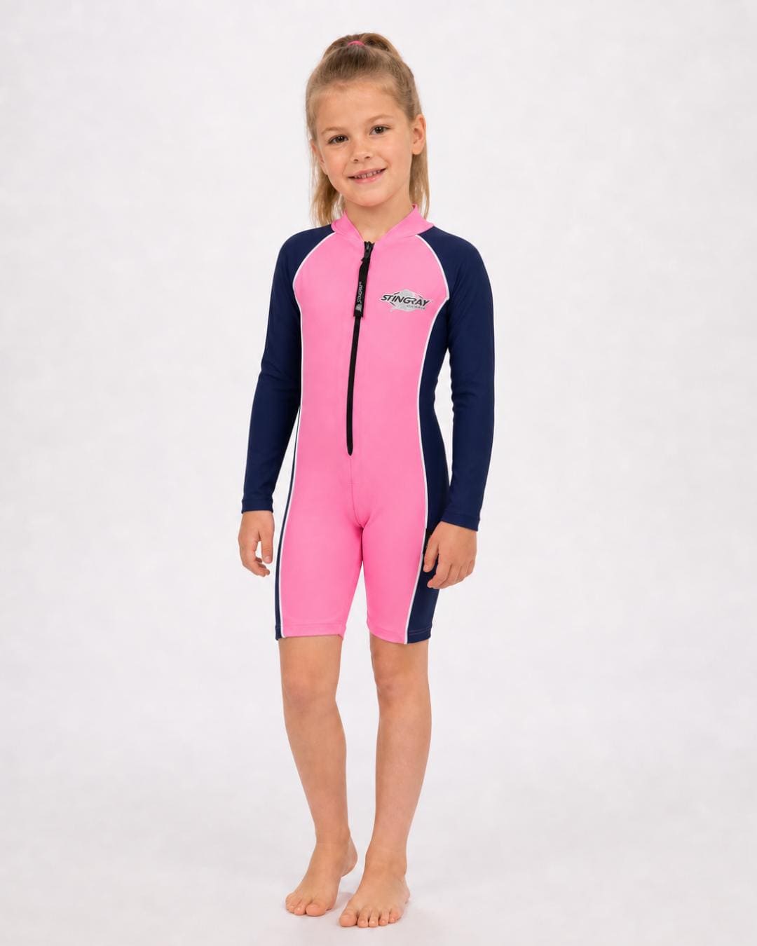 6 year old girl wearing a long sleeve UV swimsuit in pink and navy standing in a white studio