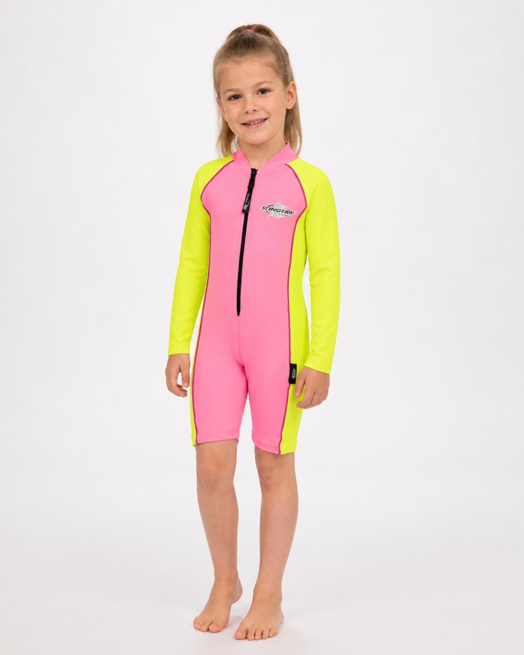 6 year old girl wearing a long sleeve UV swimsuit in pink and yellow standing in a white studio