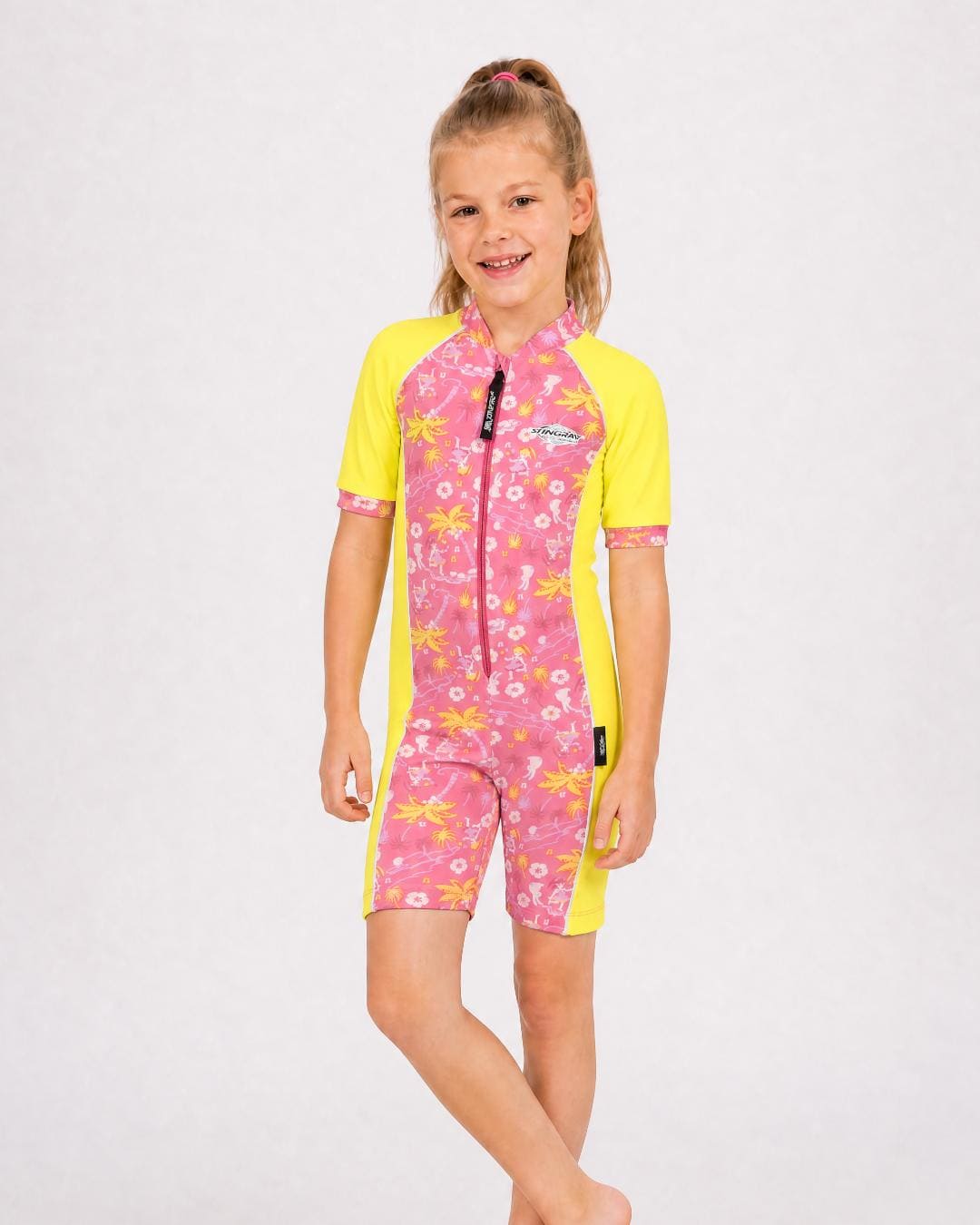 6 year old girl wearing a pink and yellow short sleeve UV swimsuit with floral patterns on a white background
