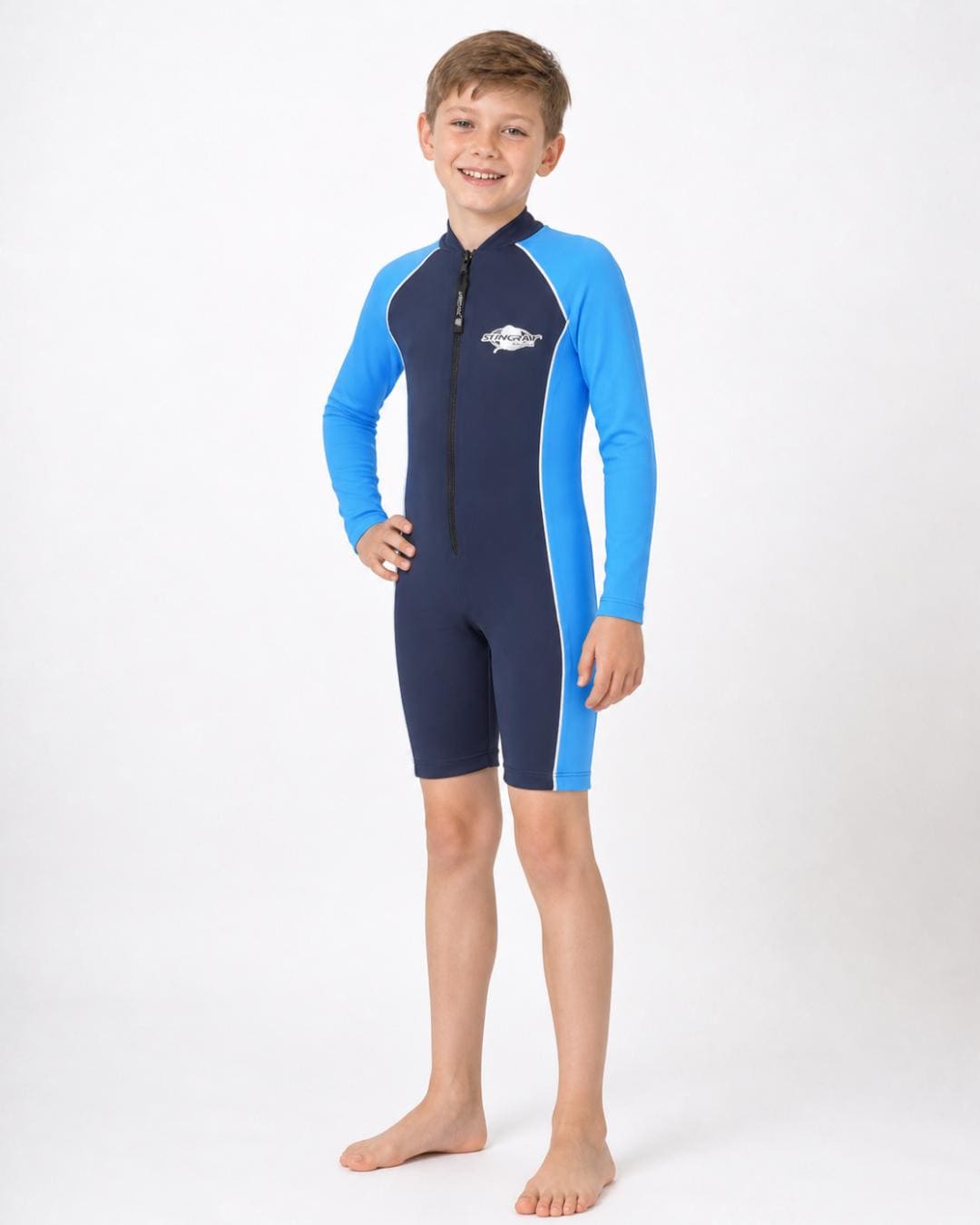 8 year old boy wearing a long sleeve UV swimsuit in navy and azure standing in a white studio