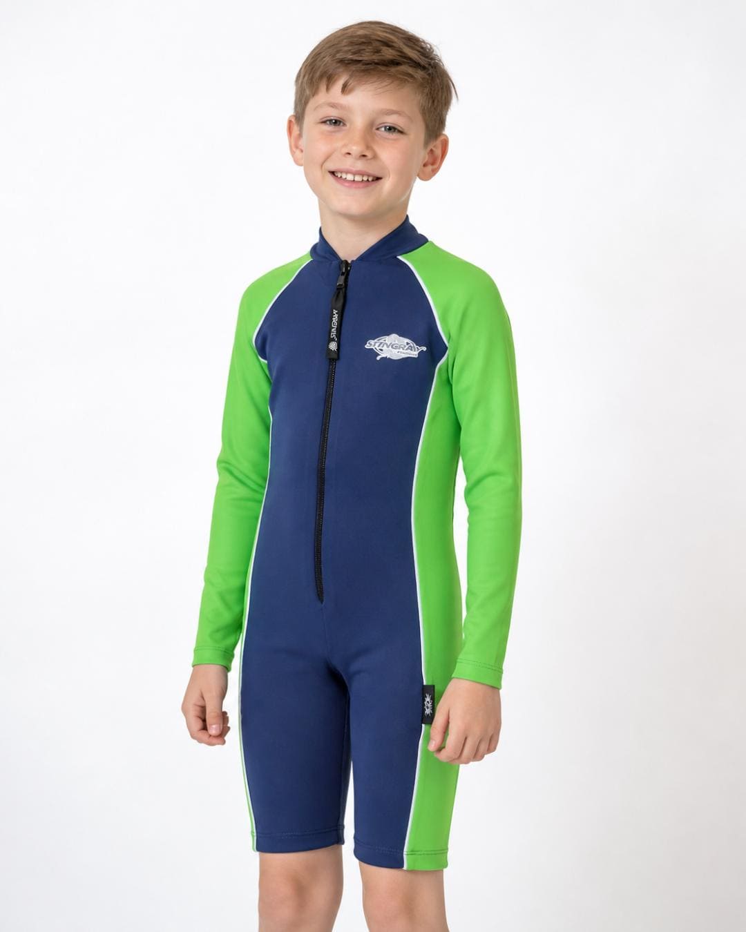 8 year old boy wearing a long sleeve UV swimsuit in navy and lime green standing in a white studio