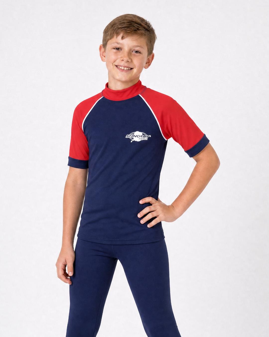8 year old boy wearing UV rash vest UPF 50+ in navy and red in a white studio