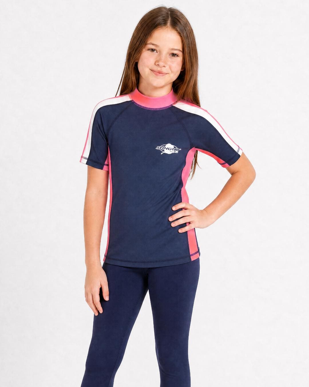 8 year old girl wearing UV rash vest UPF 50+ in navy, pink and white in a white studio