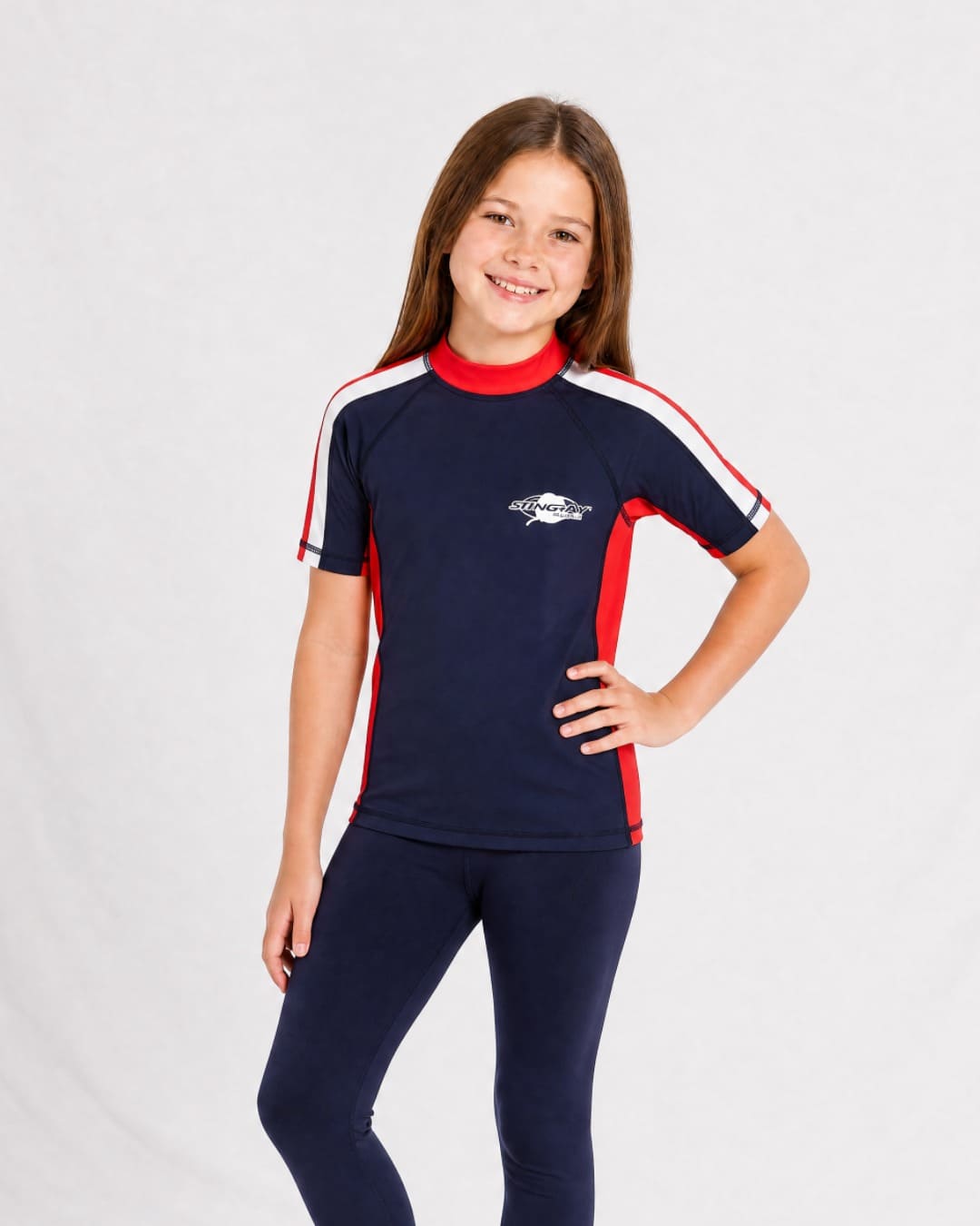 8 year old girl wearing UV rash vest UPF 50+ in navy, red and white in a white studio