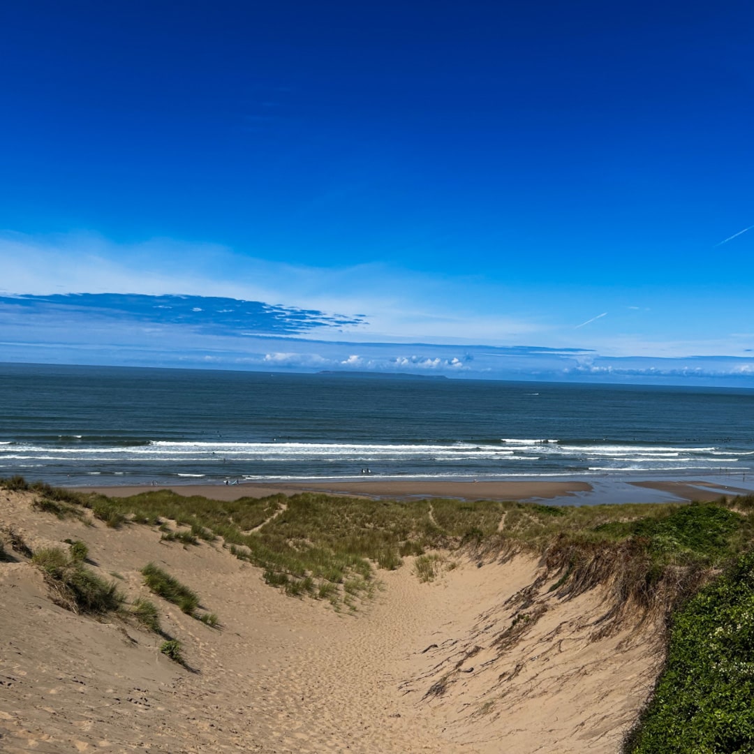 Beach scene with sand dunes, ocean waves, and clear blue sky