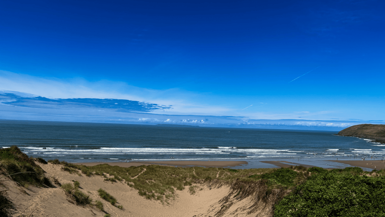Beach scene with sand dunes, ocean waves, and clear blue sky