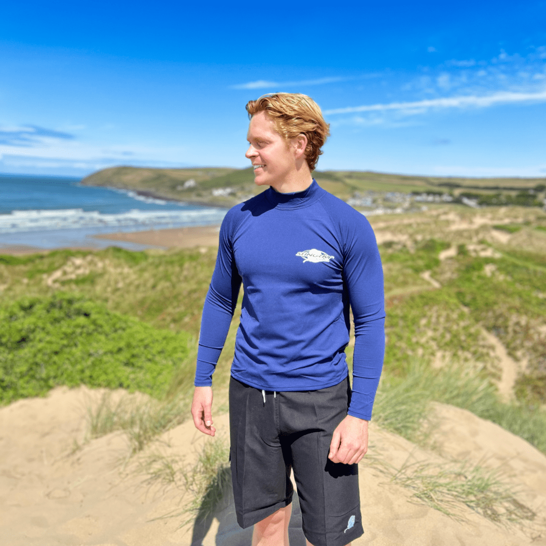Person wearing a blue UPF50+ long-sleeve shirt with a stingray logo, standing on a coastal landscape.