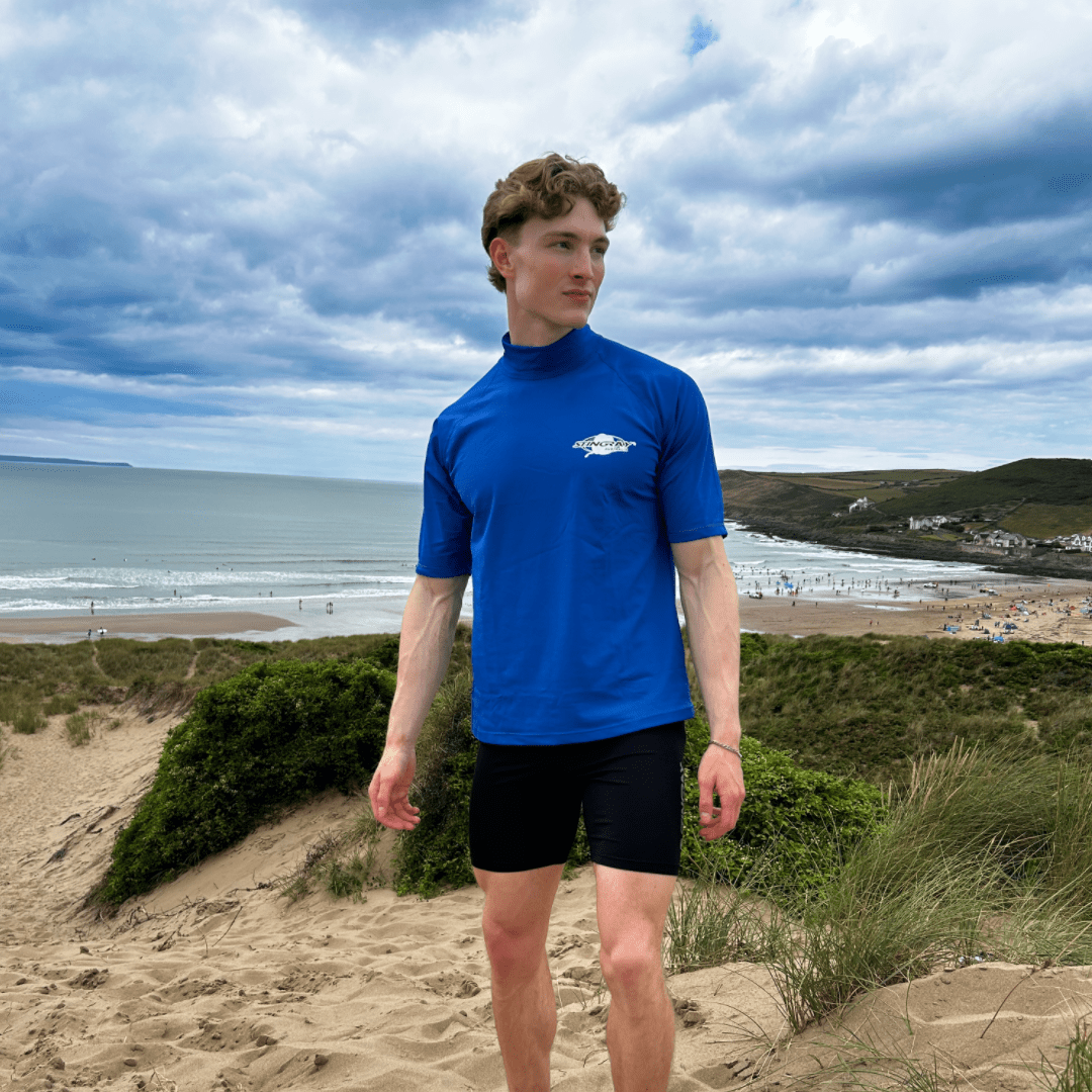 Man wearing a blue UPF 50+ swim shirt with a logo on a beach
