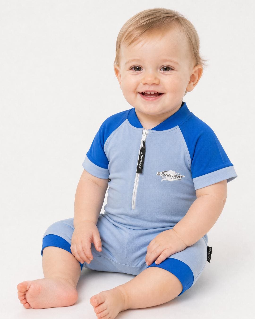 Baby wearing a blue short sleeve UV swimsuit/romper/onesie UPF 50+ on a white background