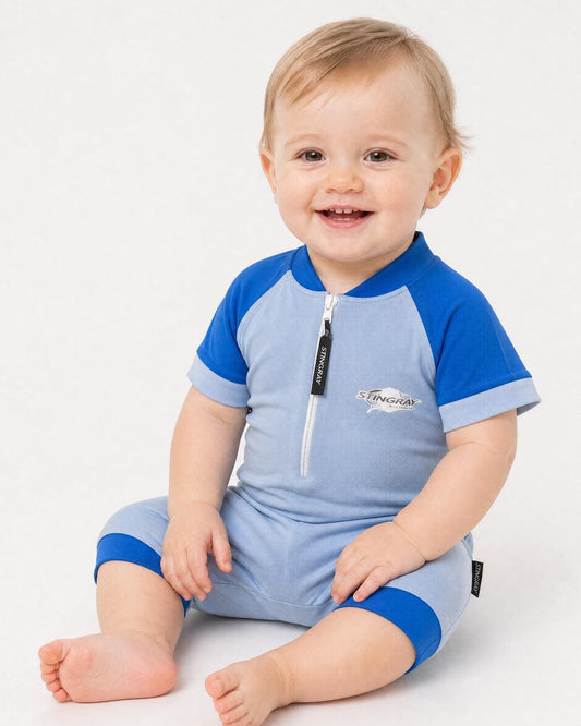 Baby wearing a blue short sleeve UV swimsuit/romper/onesie UPF 50+ on a white background