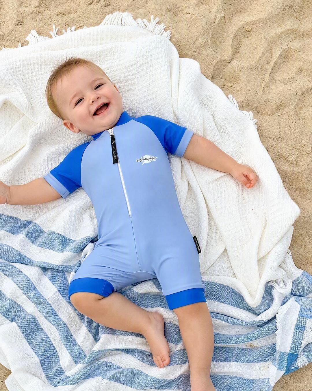 Baby wearing short sleeve UV swimsuit romper UPF 50+ - blue on the beach