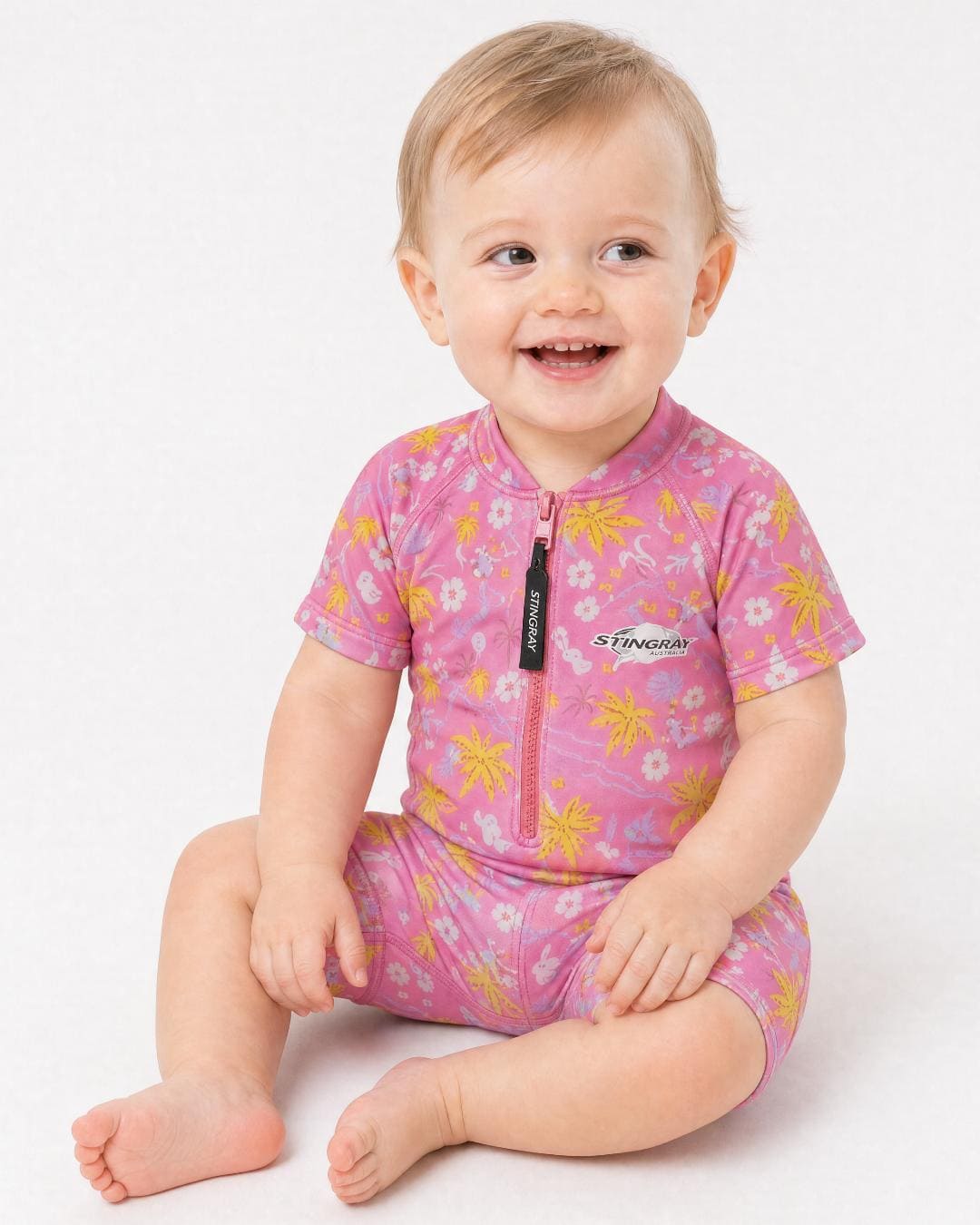 Baby wearing a pink floral short sleeve UV swimsuit/romper/onesie UPF 50+ on a white background