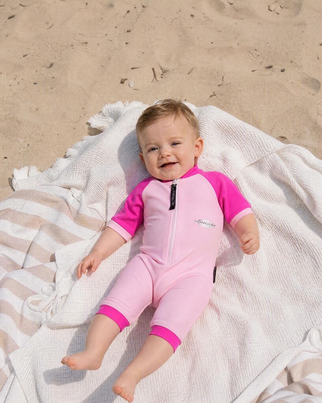 Baby wearing short sleeve UV swimsuit romper UPF 50+ - pink on the beach