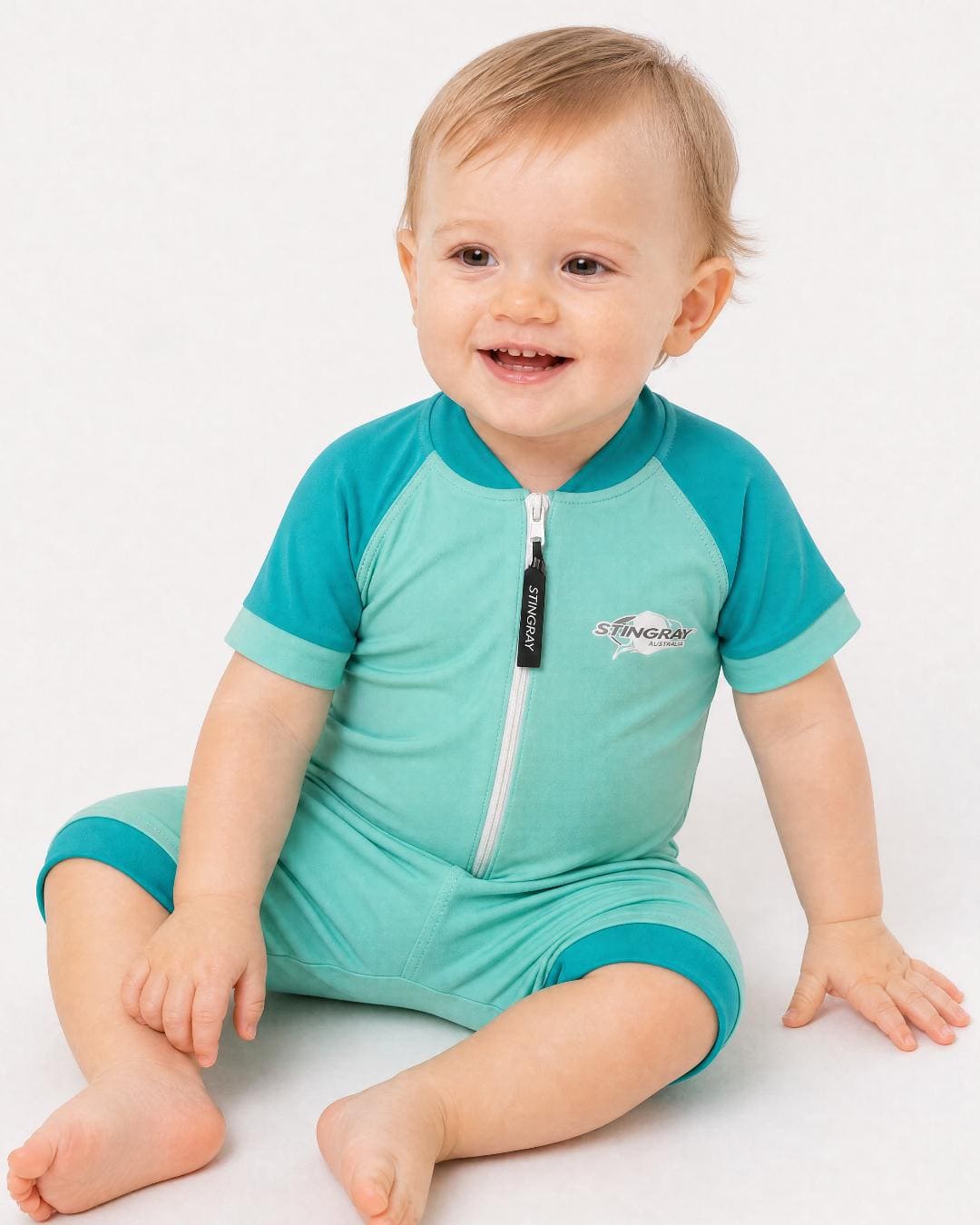 Baby wearing a teal short sleeve UV swimsuit/romper/onesie UPF 50+ on a white background