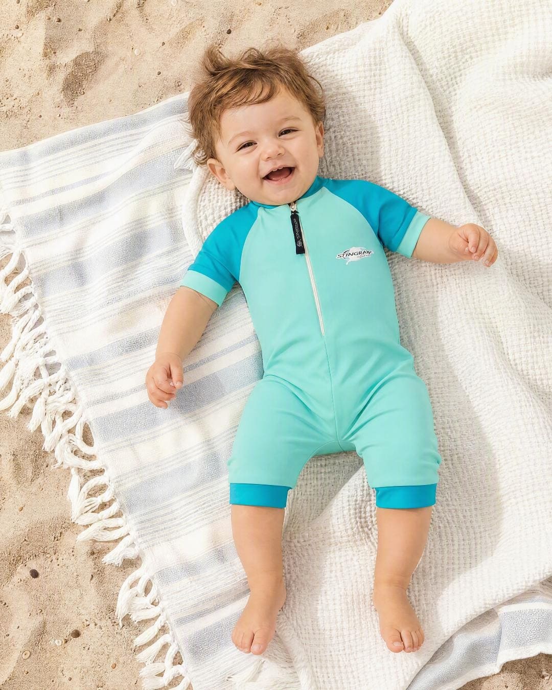 Baby wearing short sleeve UV swimsuit romper UPF 50+ - teal on the beach