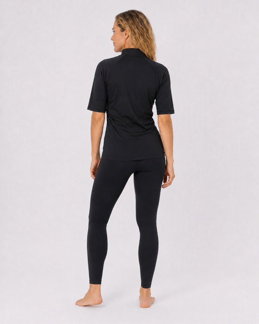 Back of Woman wearing a black short-sleeve zipped UV swim top on a white background
