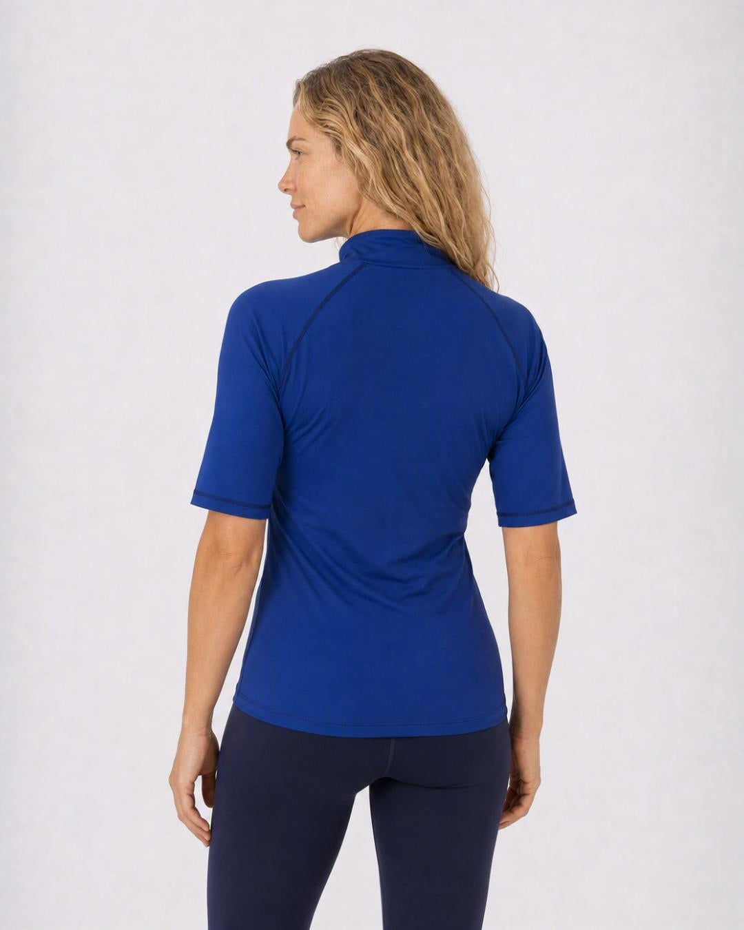Back of woman wearing a navy blue zipped UV short sleeve rash shirt on a white background