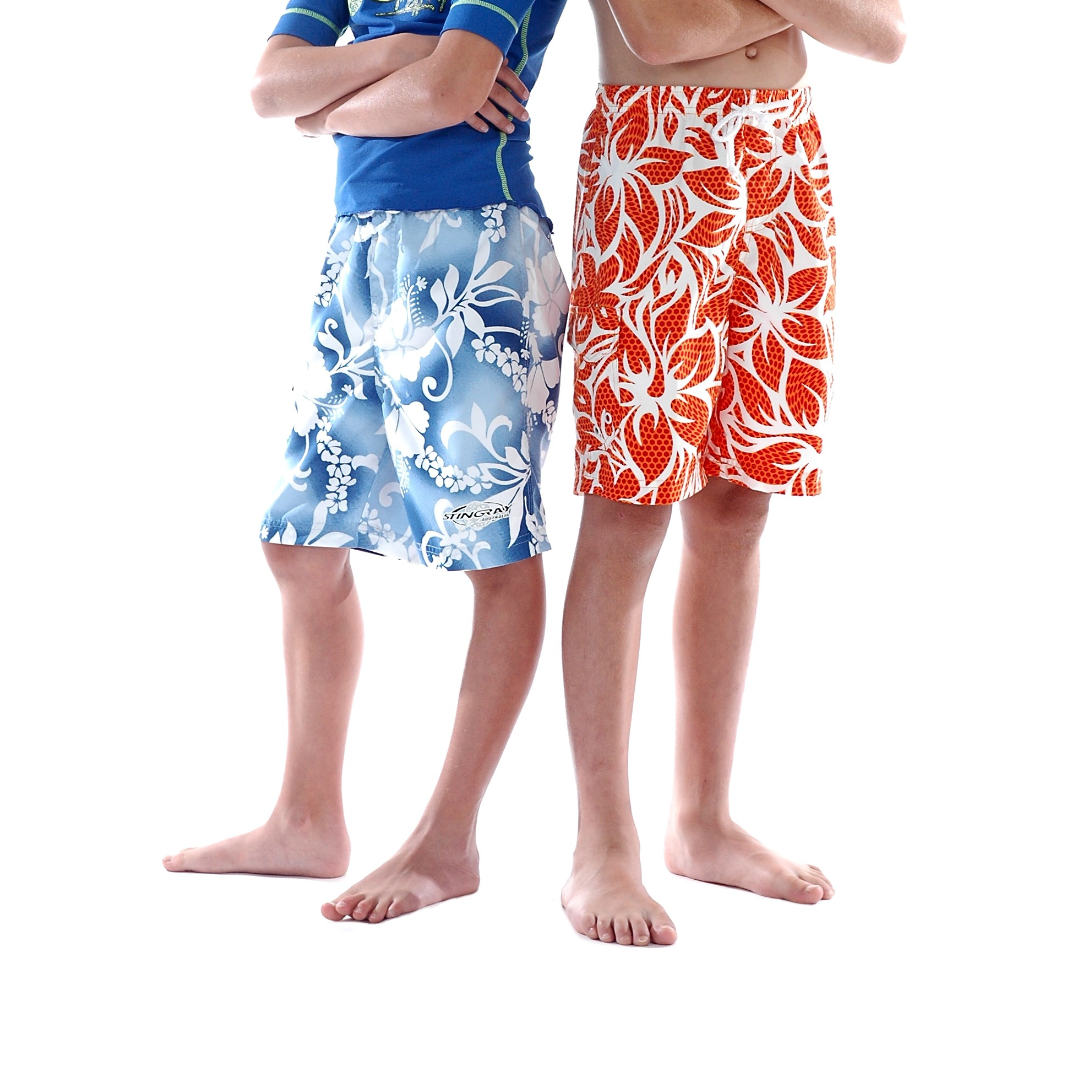 Two kids wearing the Australian-designed Stingray Kids' Unisex Hawaii Board Shorts with UPF 50+ sun protection, featuring a side pocket and drawstring. Colourways shown are blue and red hawaii patterns.