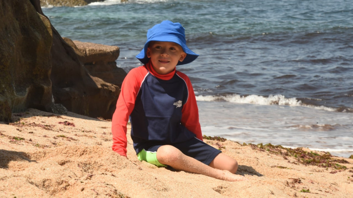 Child in a UPF 50+ sun hat and swim top on the beach