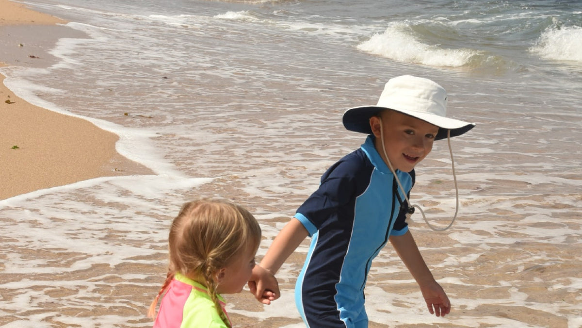 Child in a UPF 50+ wide brim sun hat and sunsuit on the beach