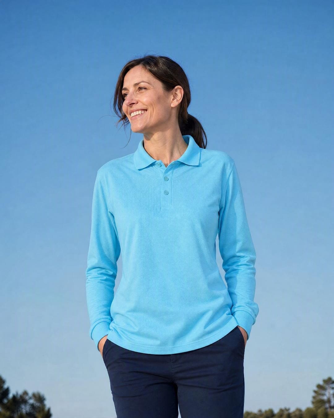 Lifestyle image of a woman wearing a blue long sleeve UV polo shirt and navy trousers