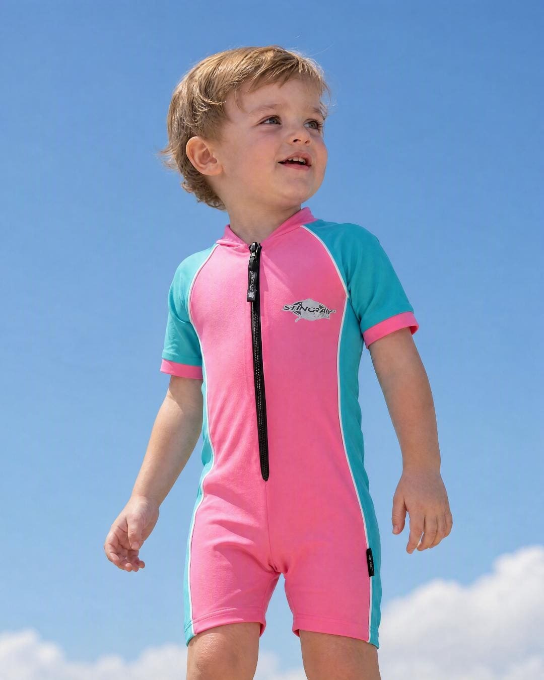 Lifestyle of 2 year old toddler wearing short sleeve UV sunsuit - pink teal