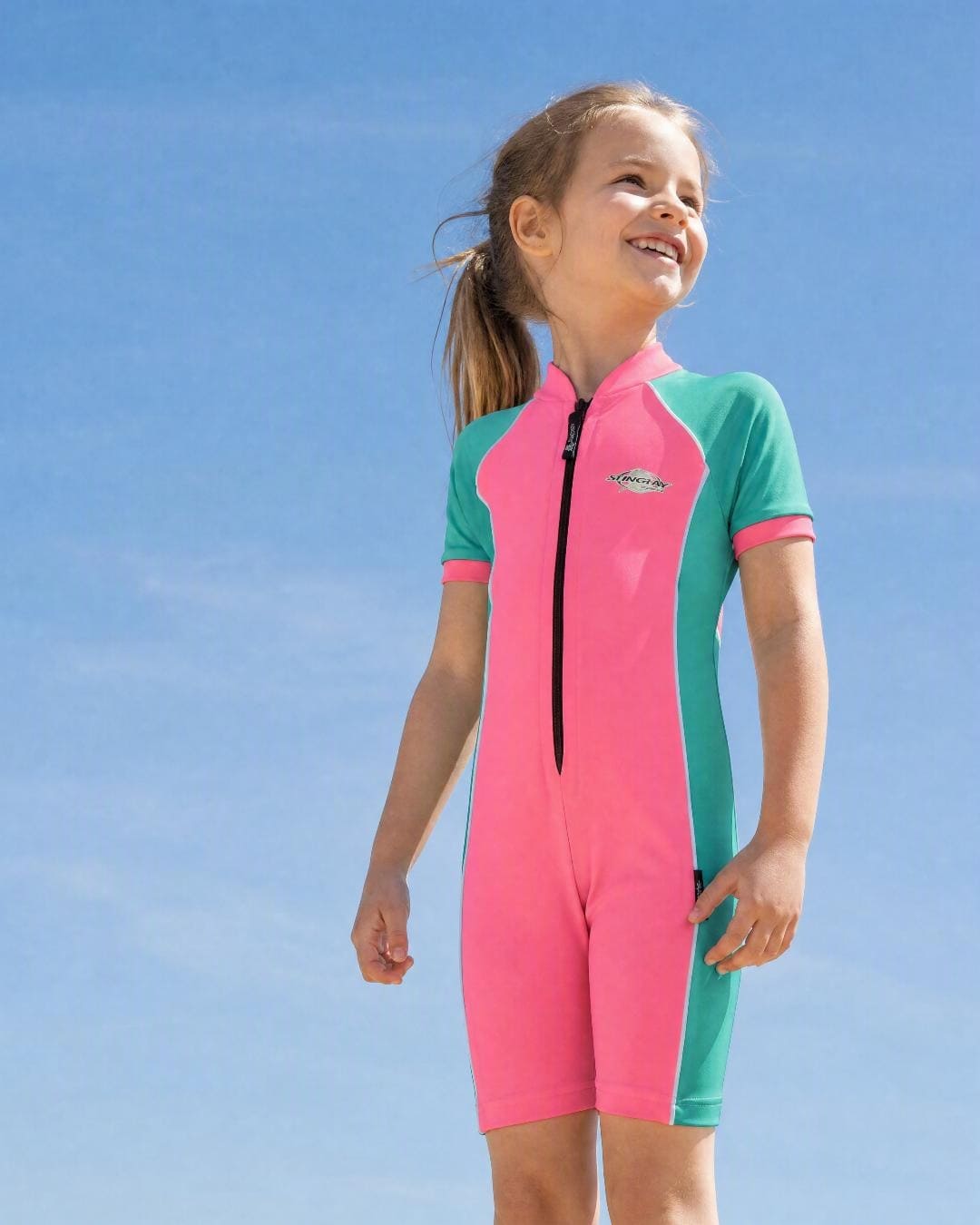 Girl wearing a kids' all-in-one short sleeve UV swimsuit UPF 50+ in pink and teal