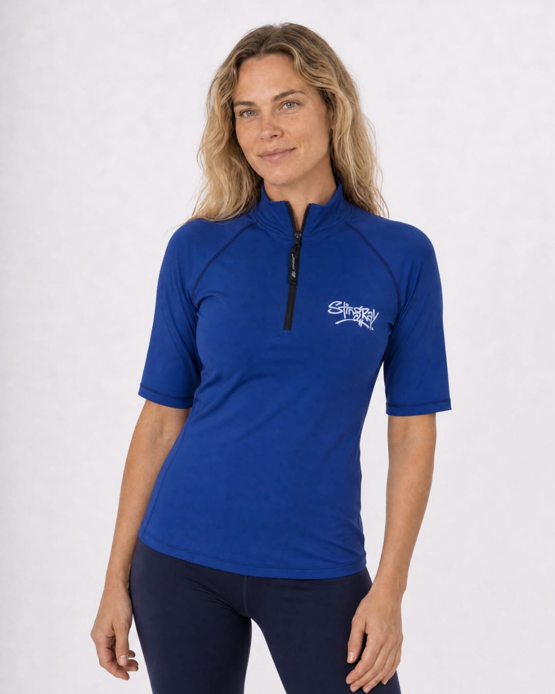 Woman wearing a navy blue zipped UV short sleeve rash shirt on a white background
