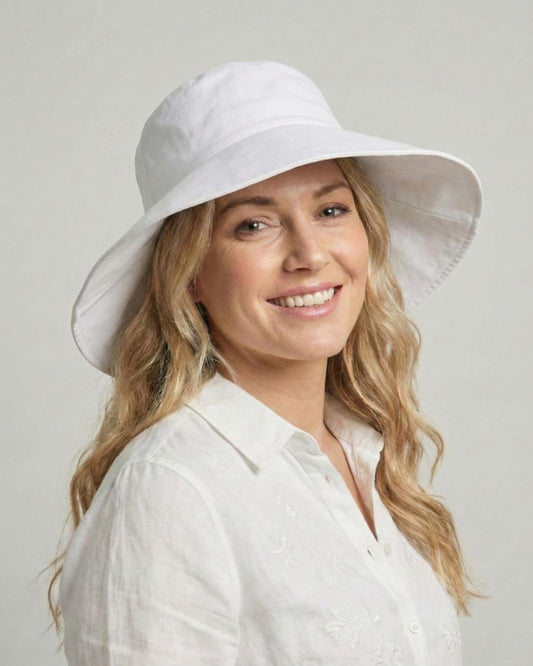 Front-facing 35-year old woman wearing wide brim white UPF 50+ sun hat in a grey studio setting