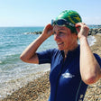 Review pic: woman wearing UPF 50+ short sleeve full-body swimsuit and triathlon goggles and hat about to go swimming