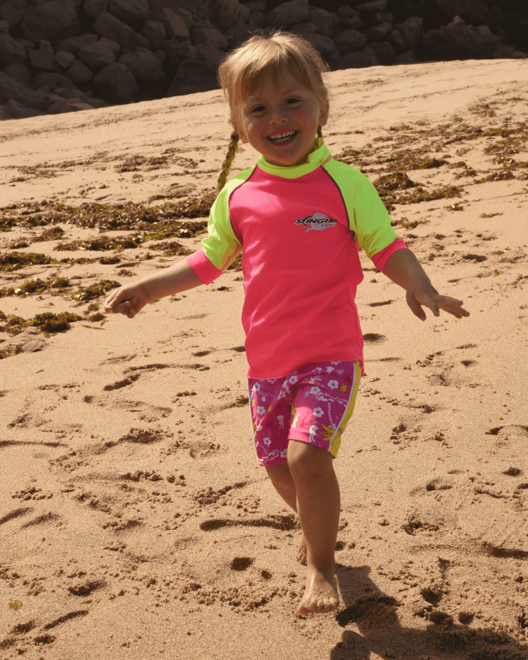 Child in a pink and yellow rash shirt on a sandy beach